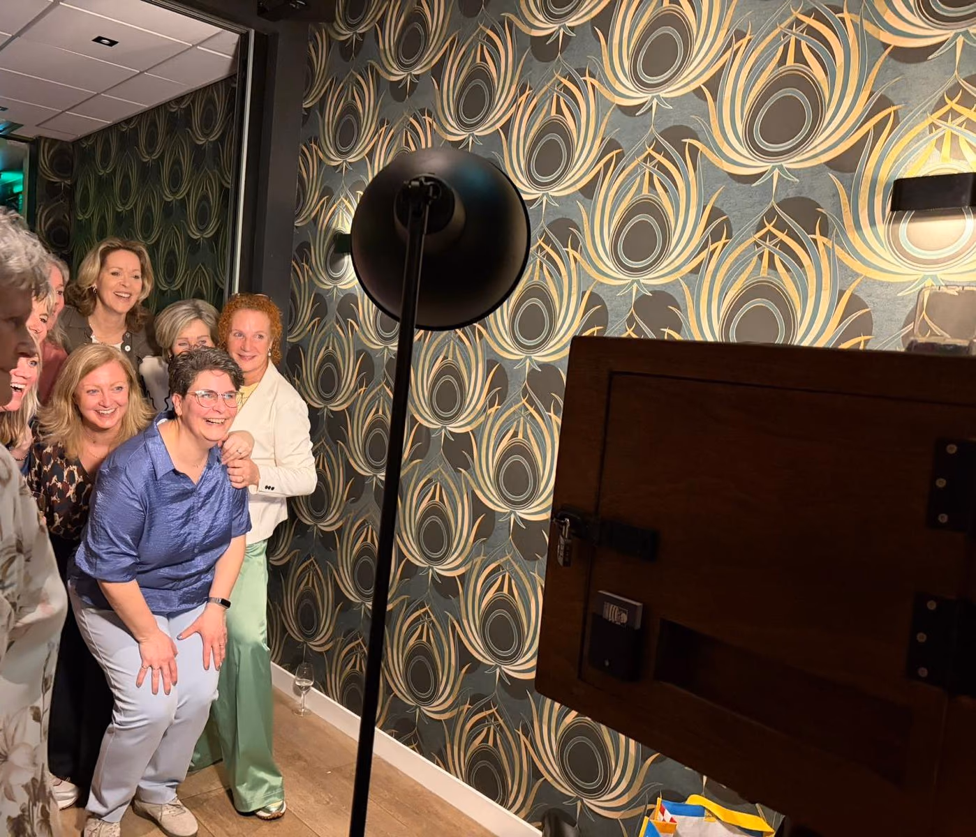 Een groep vrouwen poseert lachend voor de photobooth voor een behang met pauwenveren.