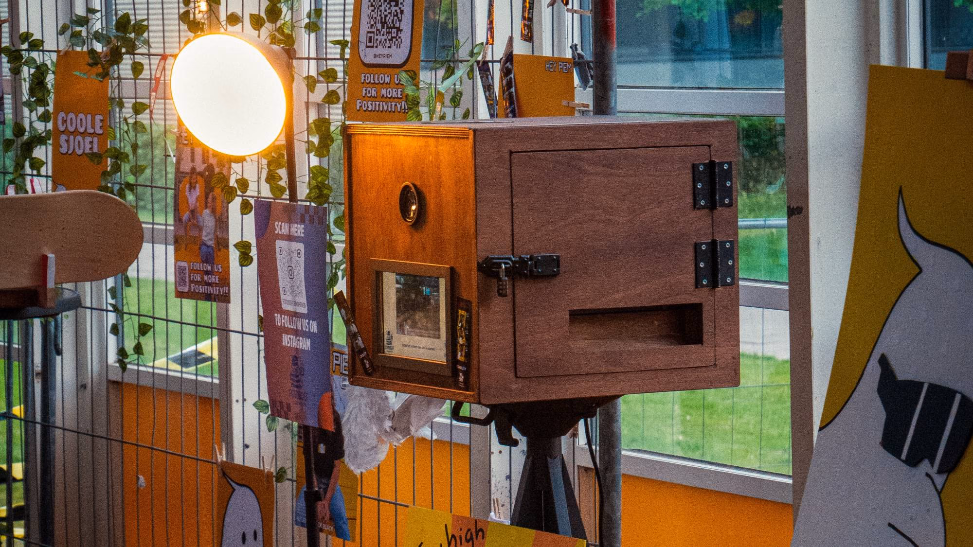 De houten photobooth op een statief naast een lamp, van de zijkant gezien.