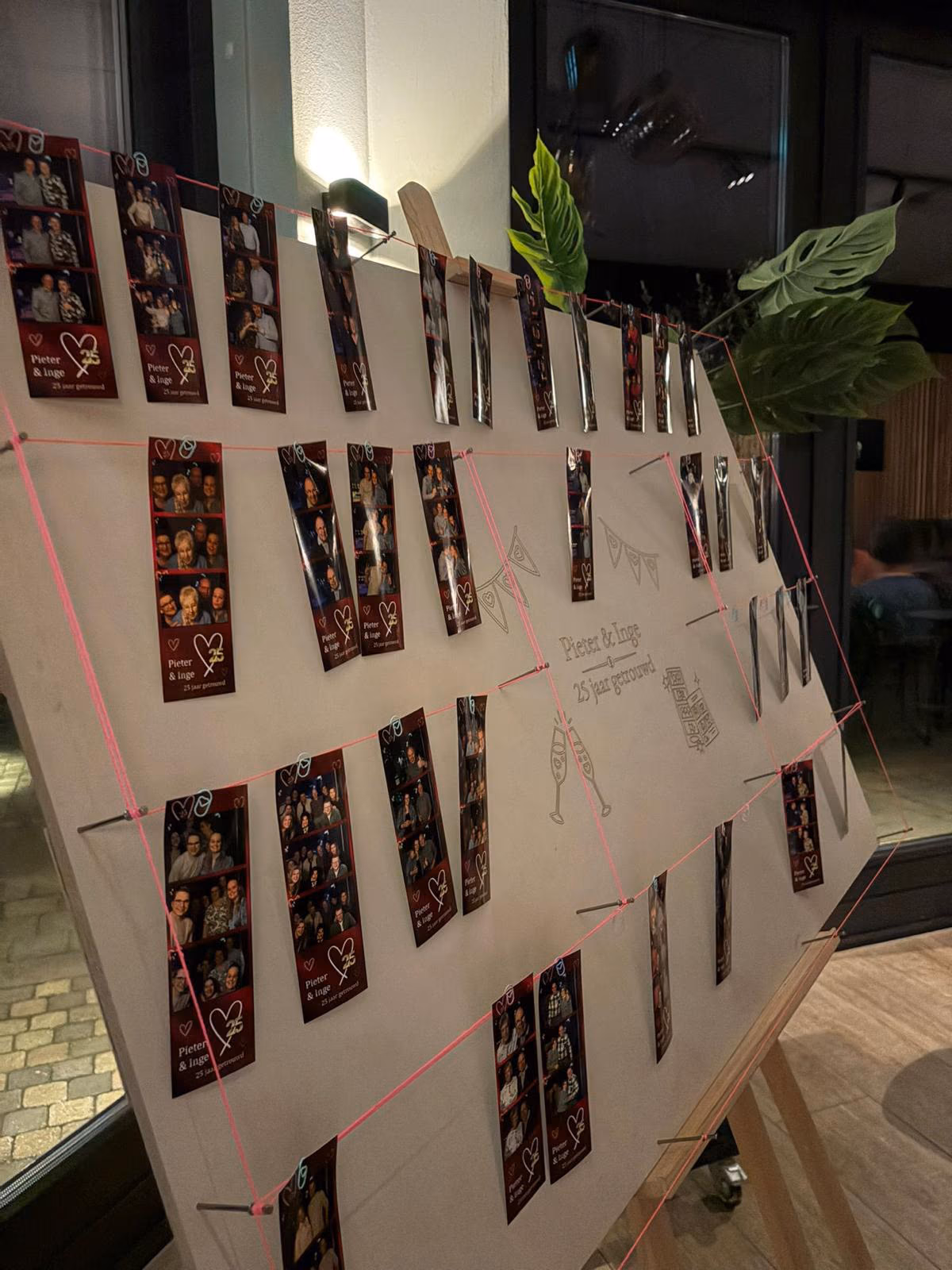 Een houten bord vol fotostrips van gasten, met de tekst Pieter & Inge, 25 jaar getrouwd.