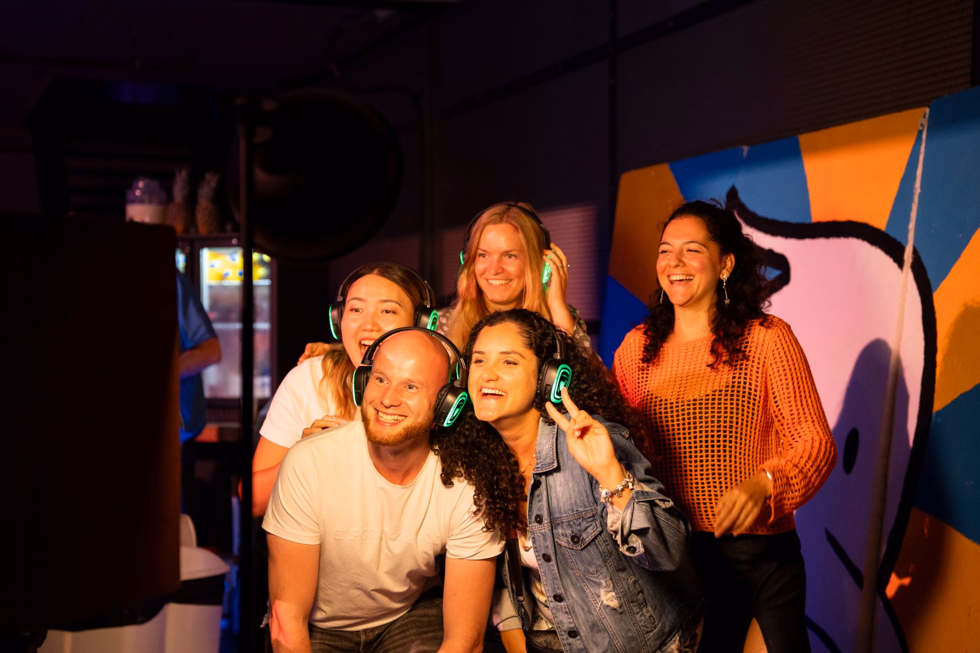 Vijf vrienden met oplichtende koptelefoons lachen in de camera van de photobooth.